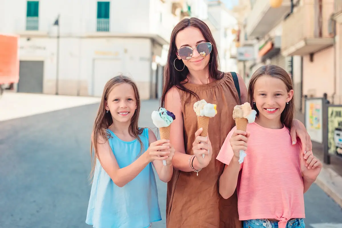 Mother with little cute daughters eating ice-cream outdoor in Italian city