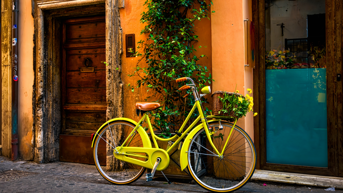 a yellow bicycle propped against an orange wall on a cobbled street in Europe