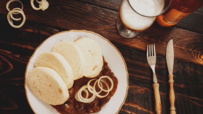 A dish of bread dumplings and goulash on a wooden table with beer