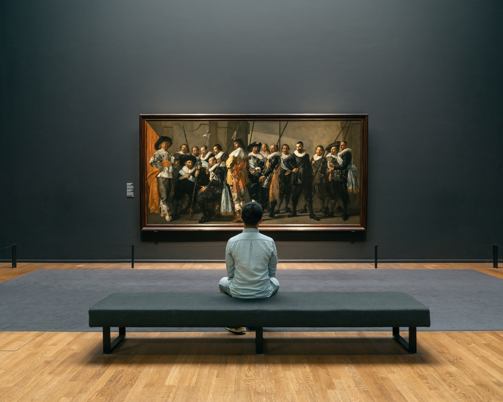 A man views an oil painting of 17th century figures at an art museum