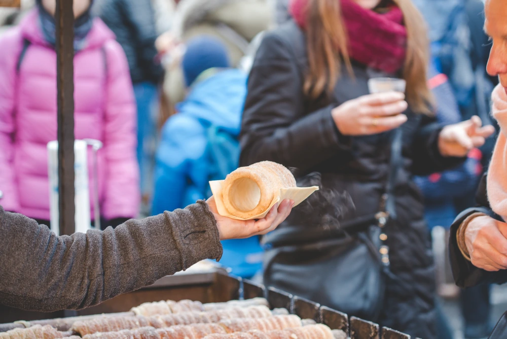 Person handing a Trdelník, a classic Czech dessert also known as Chimney Cake.